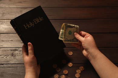 Donate and give concept. Woman with dollar banknotes, coins and Bible at wooden table, closeup