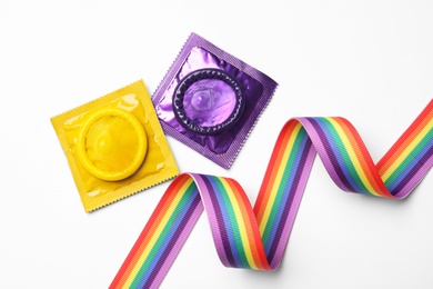 Photo of Colorful condoms and rainbow ribbon on white background, top view. LGBT concept