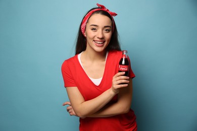 Photo of MYKOLAIV, UKRAINE - JANUARY 27, 2021: Young woman holding bottle of Coca-Cola on light blue background