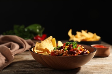 Tasty chili con carne served with tortilla chips in bowl on table