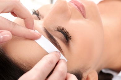 Photo of Young woman having professional eyebrow correction procedure in beauty salon