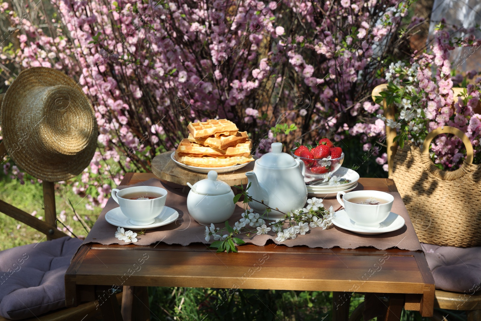 Photo of Beautiful spring flowers, freshly baked waffles and ripe strawberries on table served for tea drinking in garden