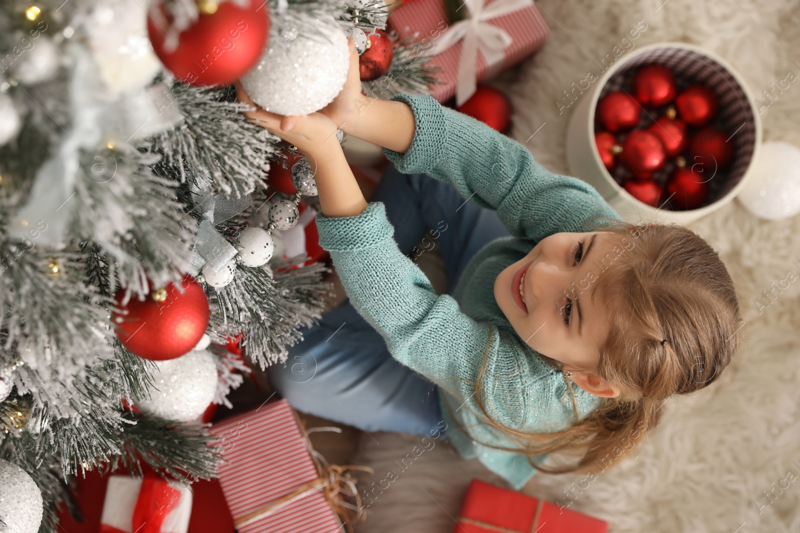 Photo of Cute little girl decorating Christmas tree at home, above view