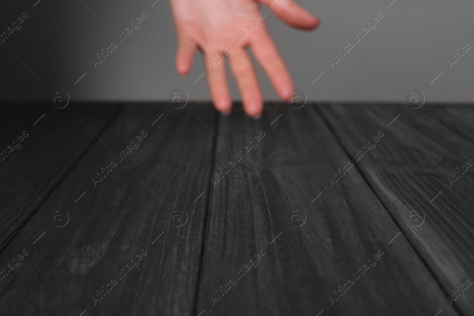 Photo of Woman holding hand above black wooden table, selective focus. Space for text