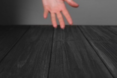 Woman holding hand above black wooden table, selective focus. Space for text