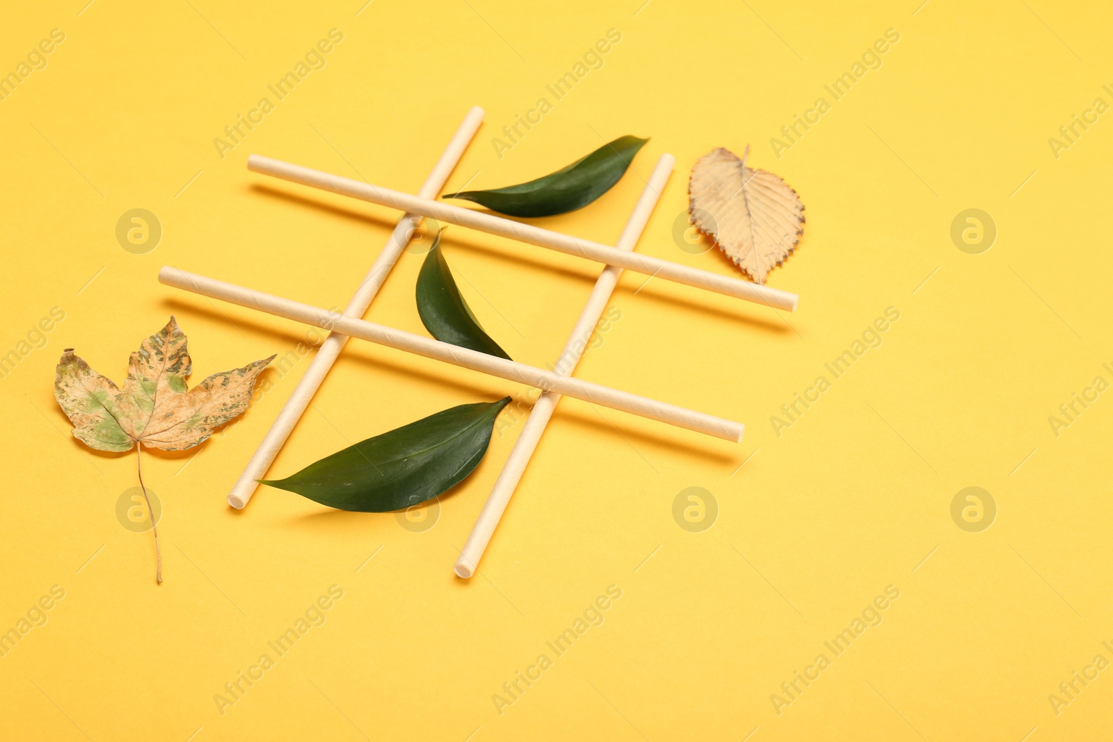 Photo of Tic tac toe game made with fresh and dry leaves on yellow background, space for text