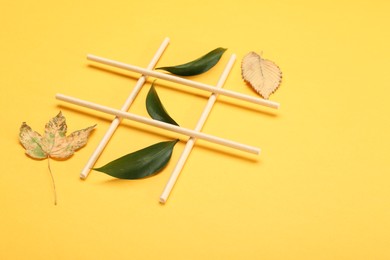 Photo of Tic tac toe game made with fresh and dry leaves on yellow background, space for text