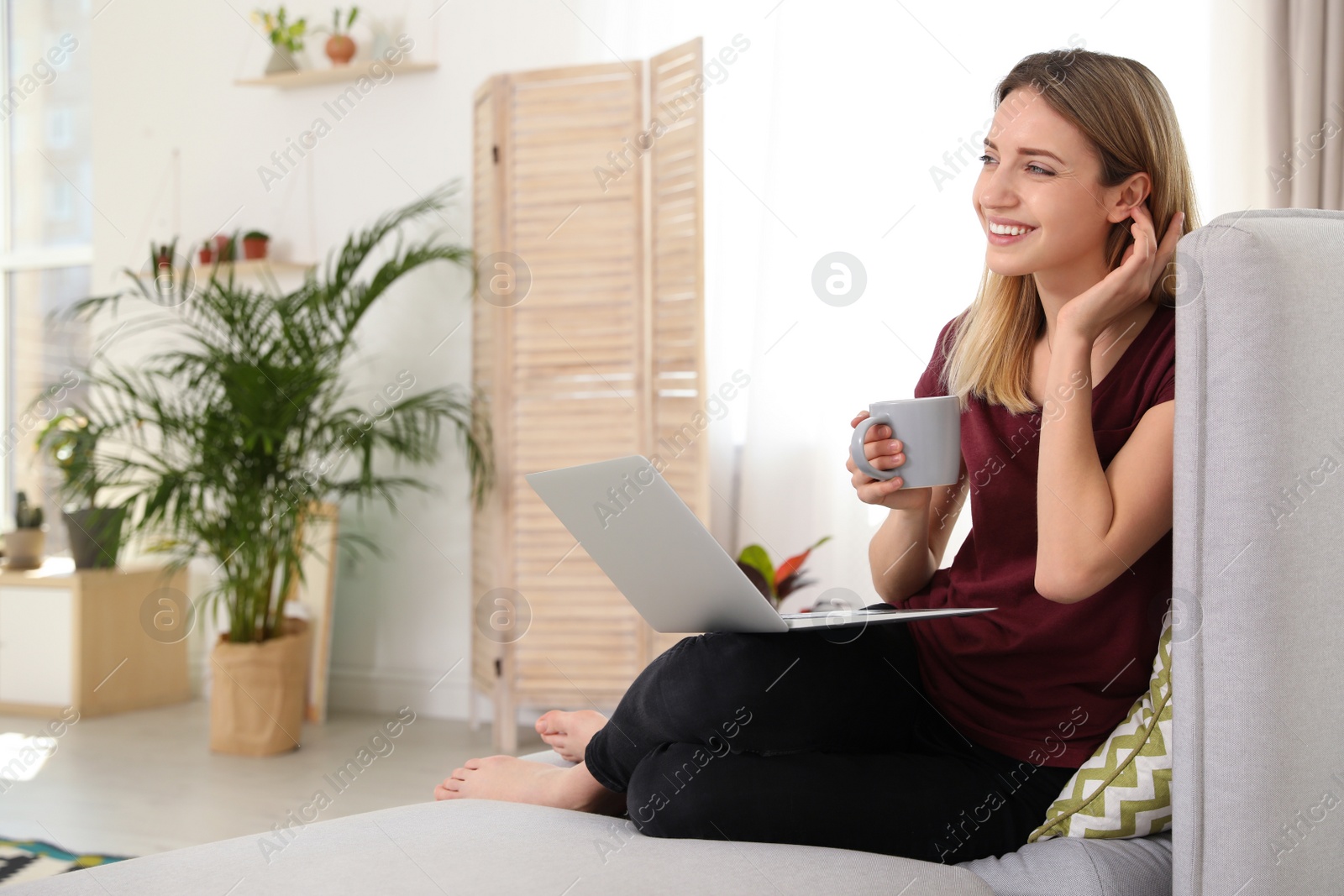 Photo of Young woman using laptop at home, space for text. Trendy room interior with plants