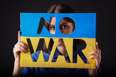 Young woman holding poster in colors of Ukrainian flag with words No War on black background