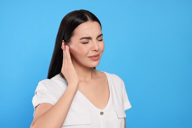 Photo of Young woman suffering from ear pain on light blue background. Space for text