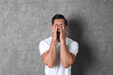 Young man being blinded and covering eyes with hands on grey background