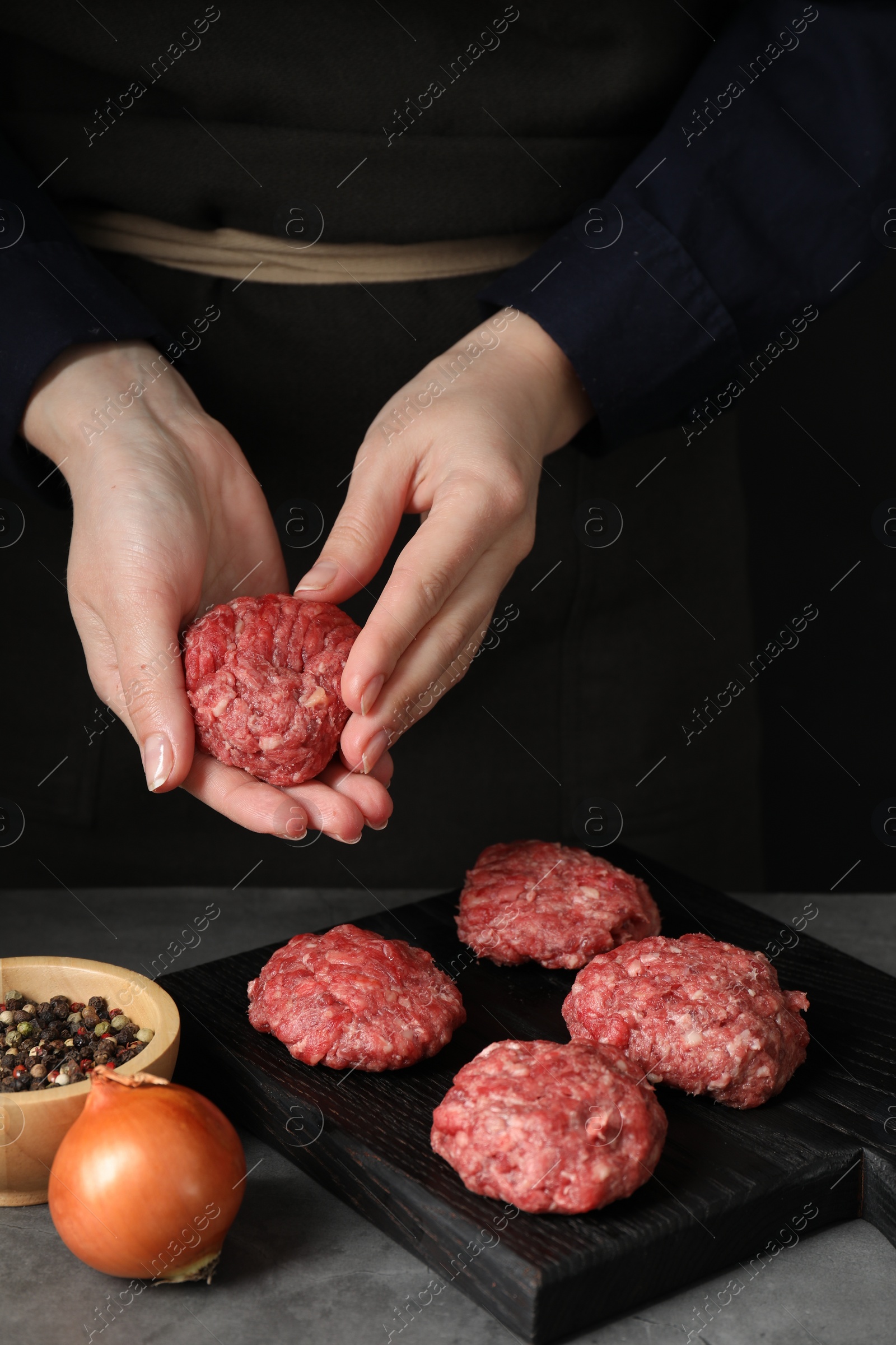 Photo of Woman making meatball from ground meat at grey table, closeup