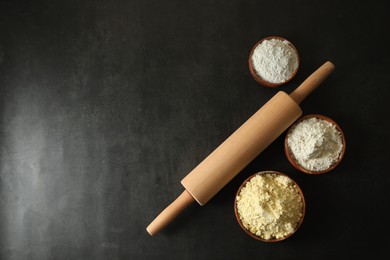 Rolling pin and different types of flour on black table, flat lay. Space for text