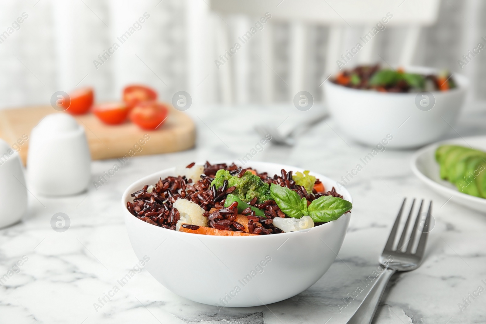 Photo of Bowl of brown rice with vegetables on table