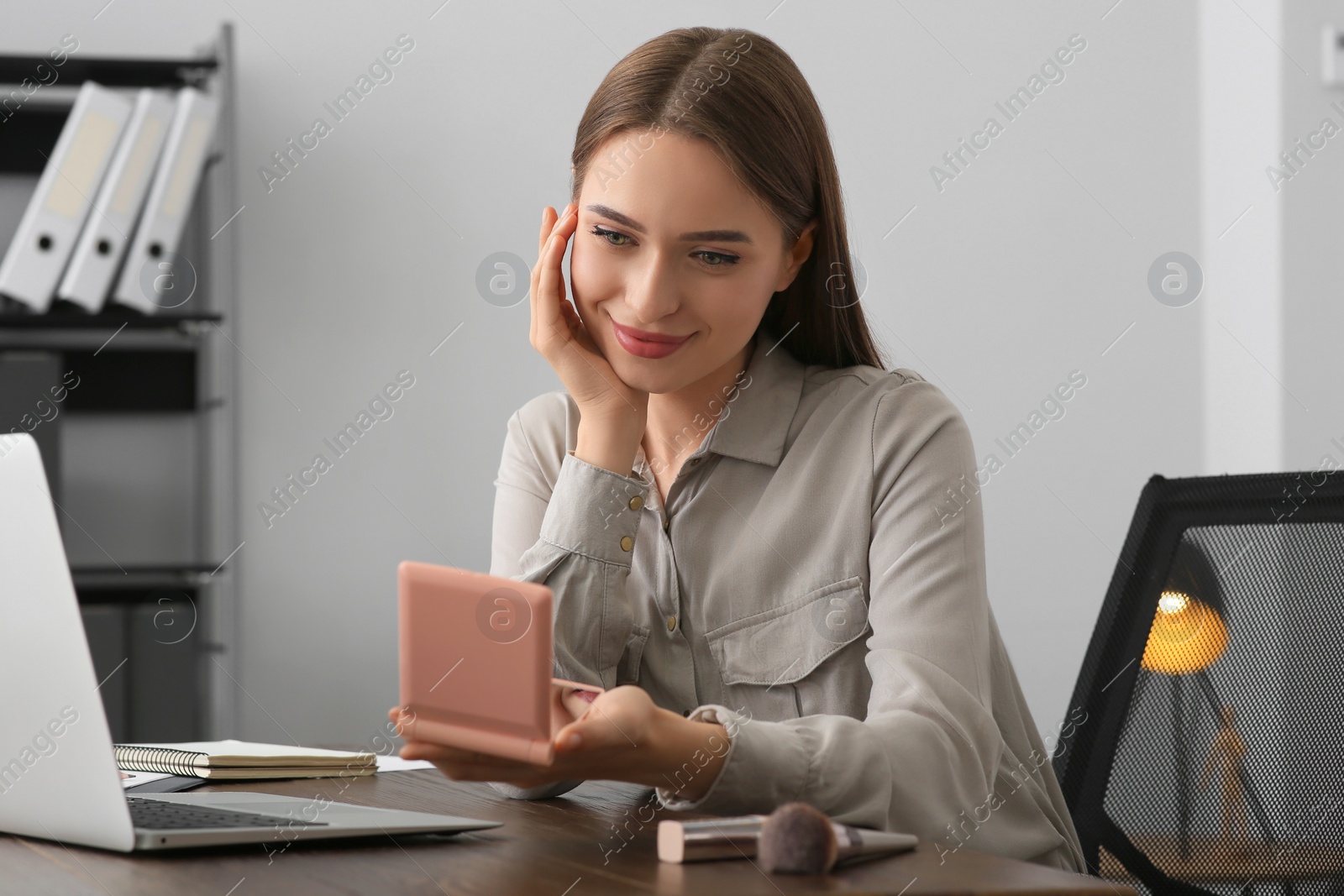 Photo of Young woman looking at herself in cosmetic pocket mirror indoors