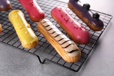 Photo of Cooling rack with different tasty glazed eclairs on grey table, closeup