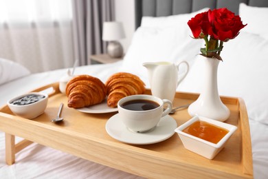 Photo of Tasty breakfast served in bed. Fresh croissants, coffee, jam and honey on wooden tray