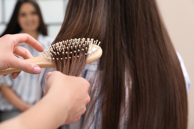 Woman combing friend's hair with cushion brush indoors, closeup