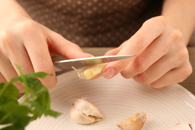 Photo of Woman peeling fresh garlic at table, closeup