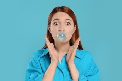 Photo of Surprised woman blowing bubble gum on turquoise background