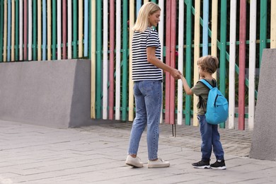 Woman and her little son on their way to kindergarten outdoors, back view. Space for text