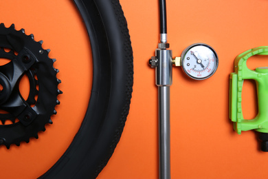 Set of different bicycle parts and manometer on orange background, flat lay