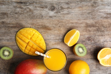 Glass with fresh mango juice and tasty fruits on wooden table, flat lay. Space for text