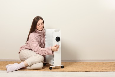 Photo of Young woman adjusting temperature on modern electric heater near beige wall, space for text