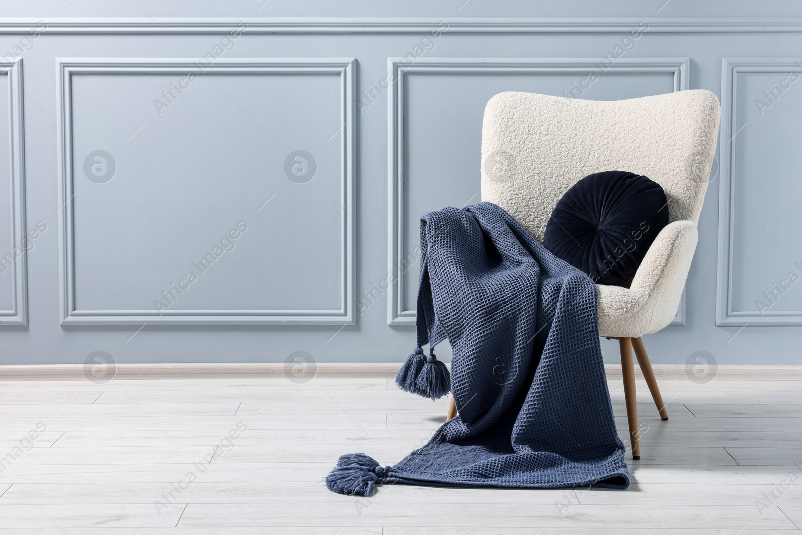 Photo of Comfortable armchair with blanket and pillow near grey wall indoors, space for text