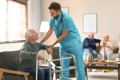Photo of Medical worker taking care of elderly man with walker in geriatric hospice