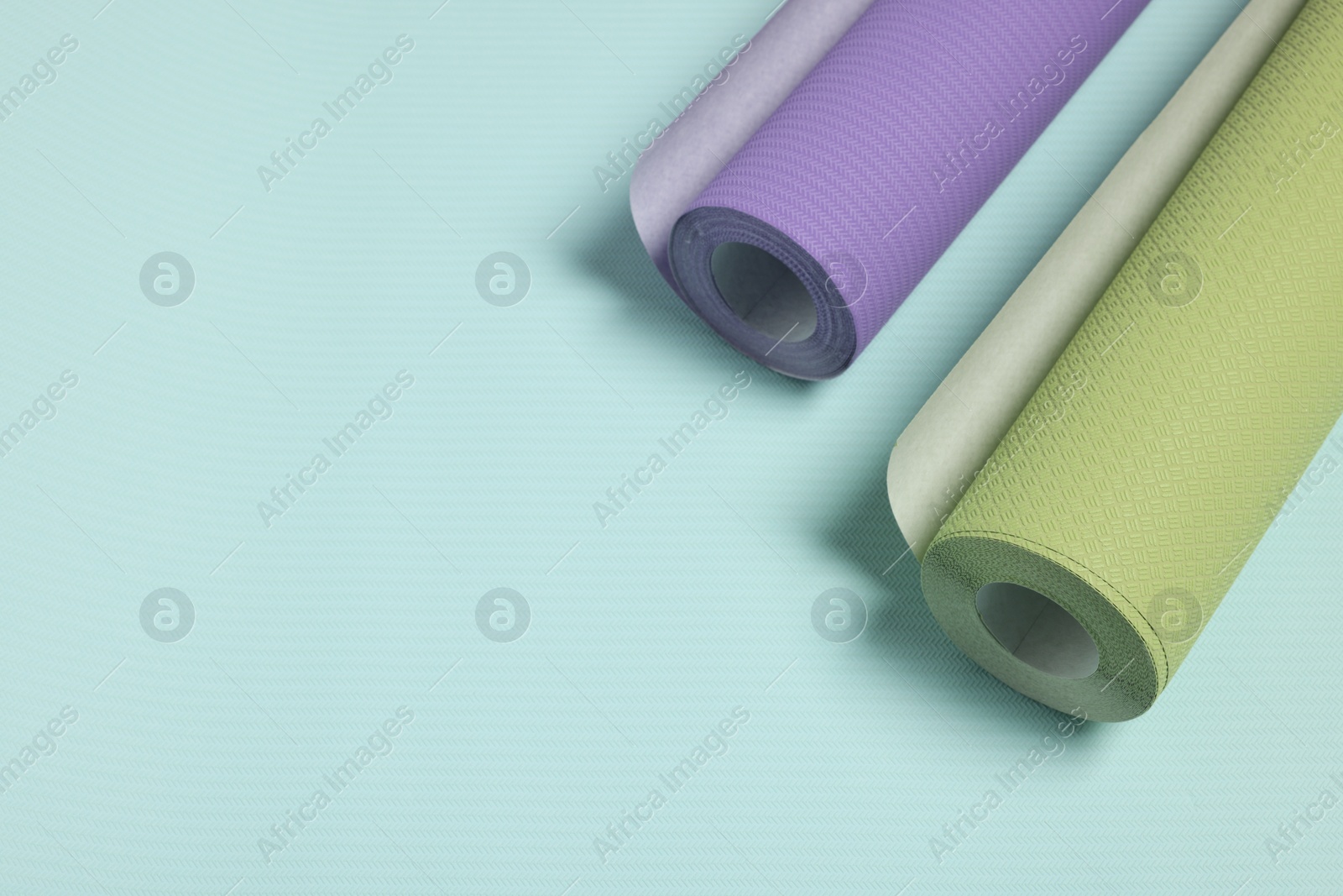 Photo of Two colorful wallpaper rolls on light turquoise sample, above view. Space for text