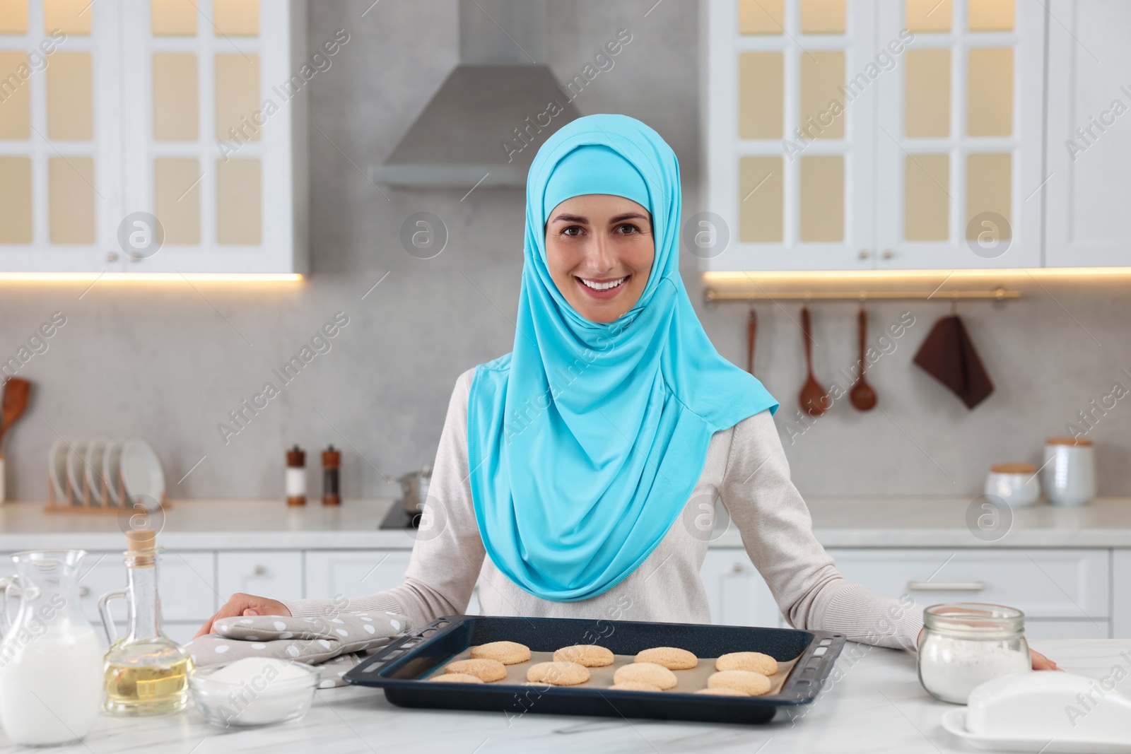 Photo of Portrait of Muslim woman near tray with cookies at white table in kitchen