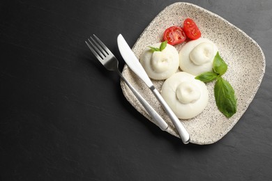 Photo of Delicious burrata cheese with basil and cut tomato on black table, top view. Space for text