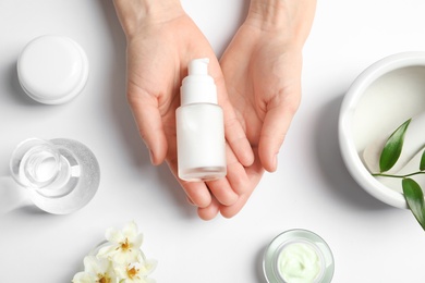 Woman holding bottle of cream over table with cosmetic products