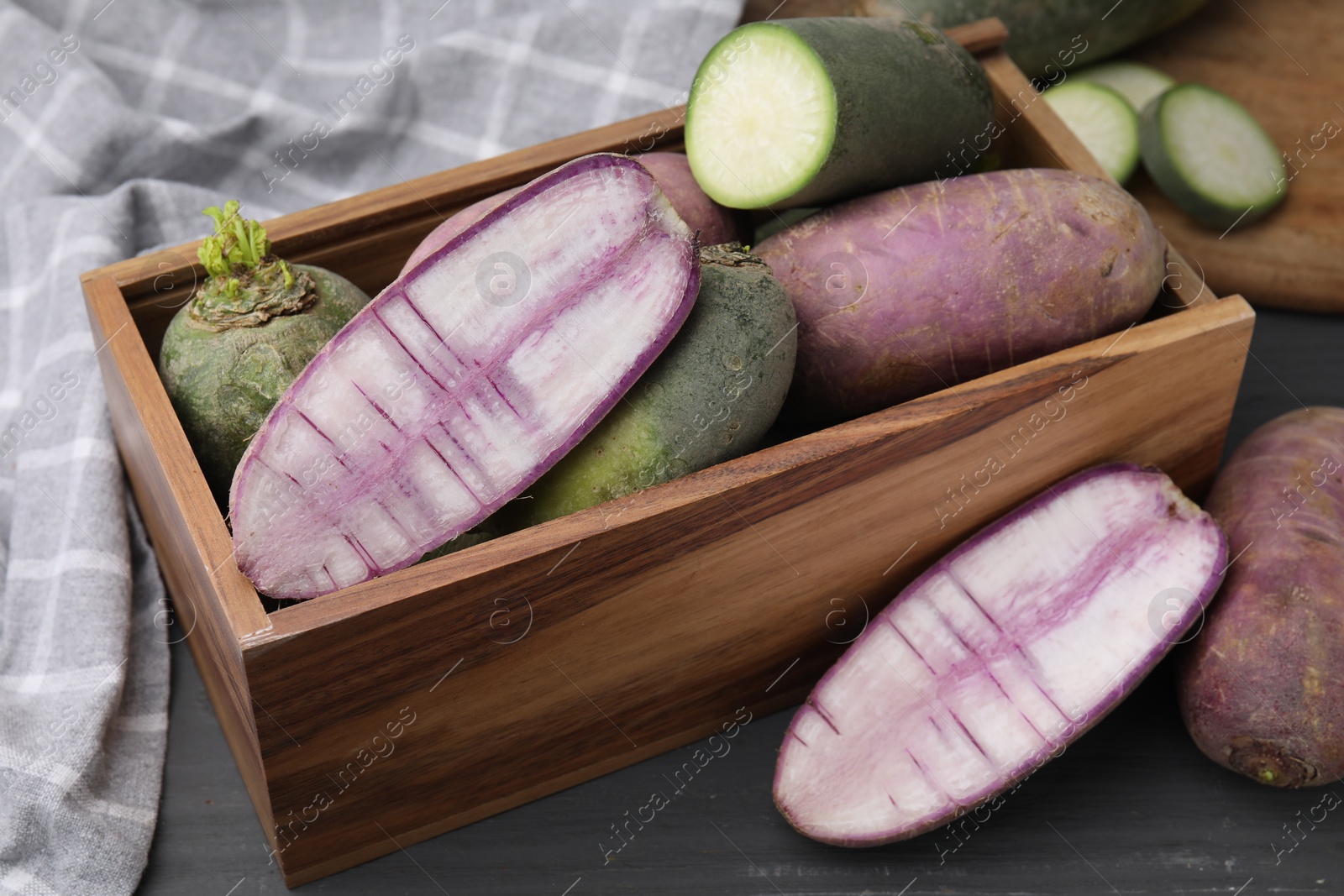 Photo of Purple and green daikon radishes in crate on black wooden table