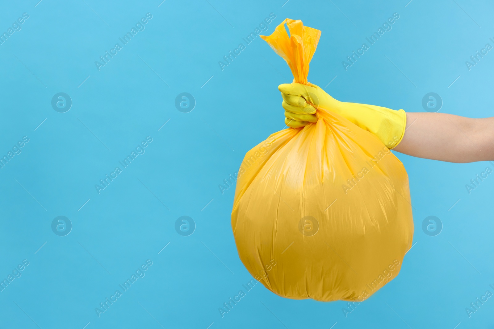 Photo of Woman holding plastic bag full of garbage on light blue background, closeup. Space for text