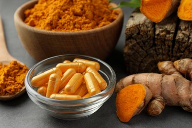 Aromatic turmeric powder, root and pills on grey table, closeup