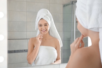 Young woman wrapped in towels near bathroom mirror. Using soap