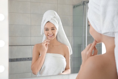 Photo of Young woman wrapped in towels near bathroom mirror. Using soap