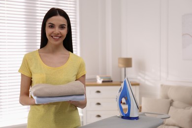 Photo of Woman with folded clothes near ironing board at home. Space for text