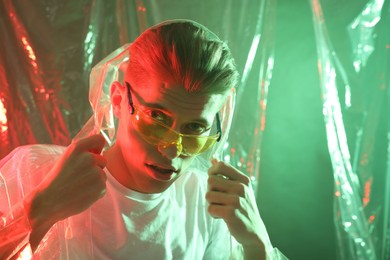 Photo of Stylish young man wearing clear coat and glasses in neon lights. Space for text