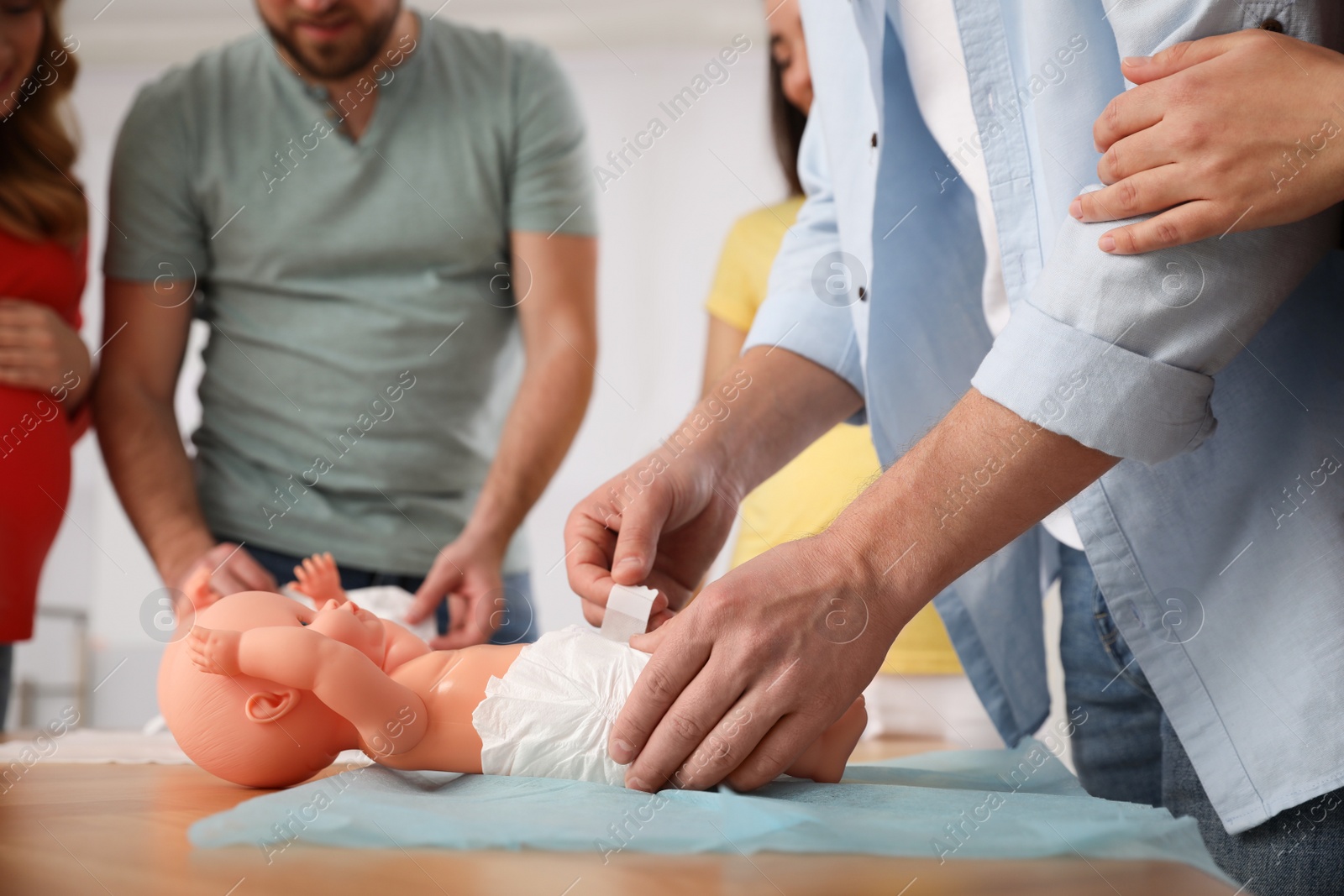 Photo of Future fathers and pregnant women learning how to swaddle baby at courses for expectant parents indoors, closeup