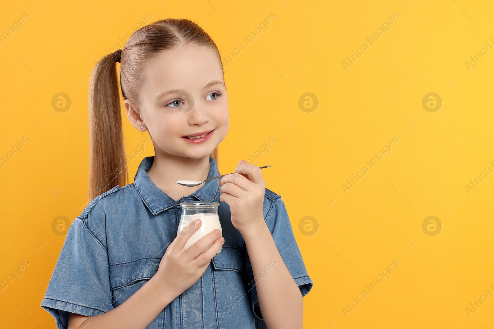 Photo of Cute little girl with tasty yogurt on orange background, space for text