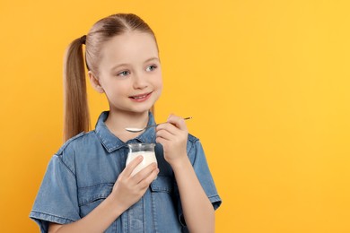 Photo of Cute little girl with tasty yogurt on orange background, space for text
