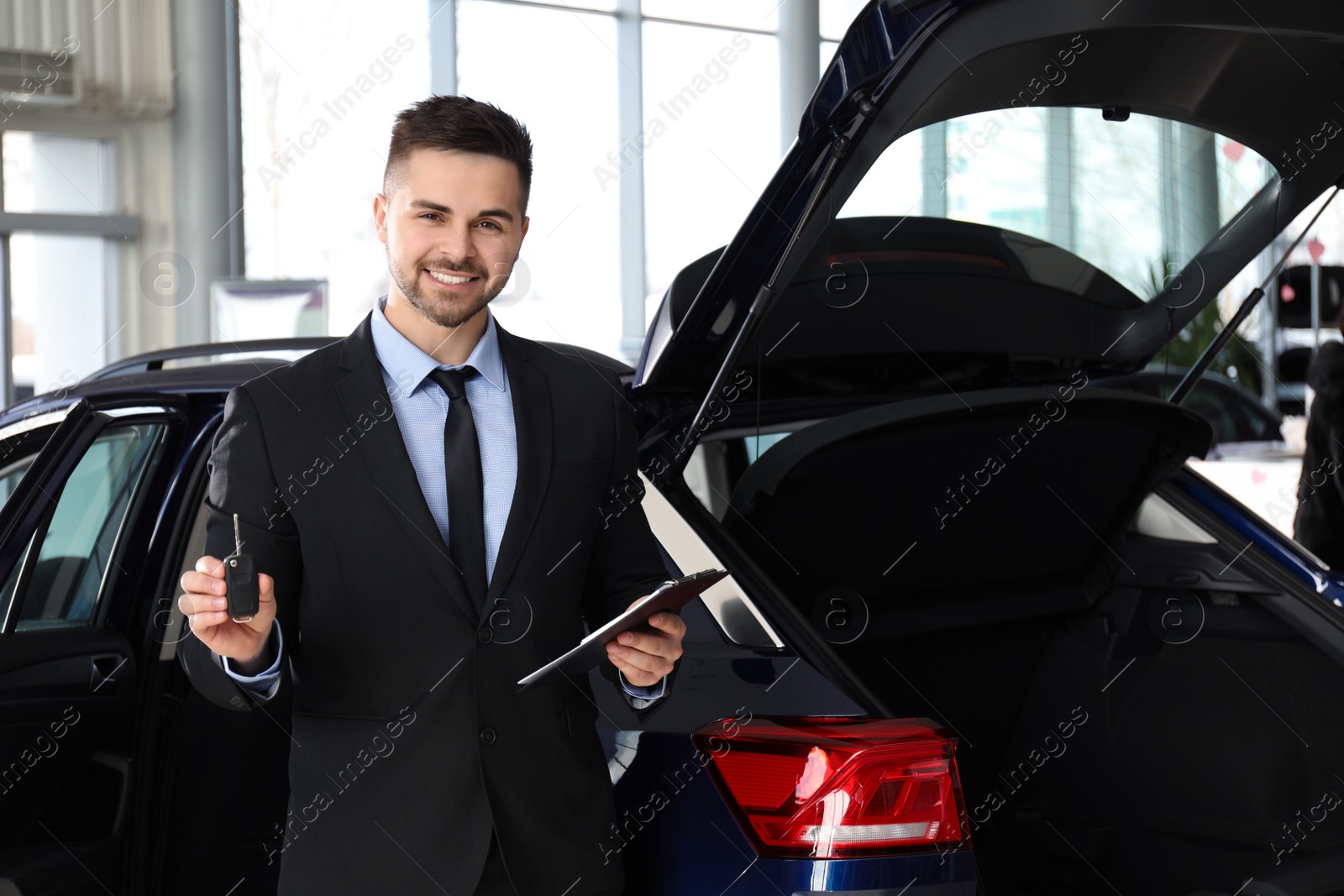 Photo of Salesman with key and clipboard near car in dealership