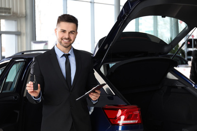 Salesman with key and clipboard near car in dealership