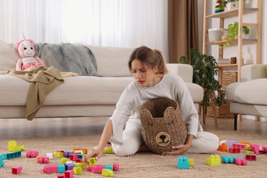 Photo of Tired young mother sitting on floor in messy living room