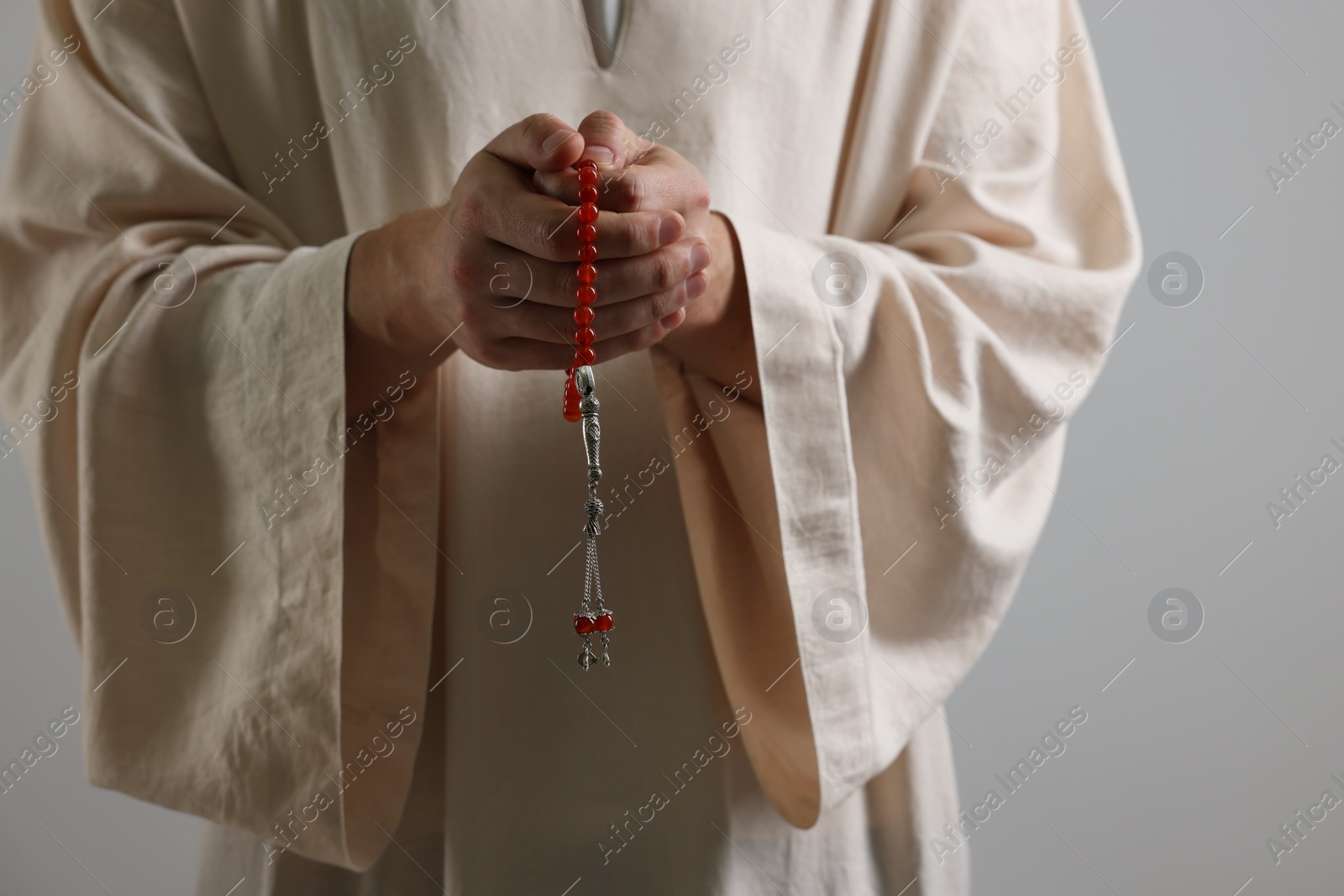 Photo of Muslim man with misbaha praying on light grey background, closeup