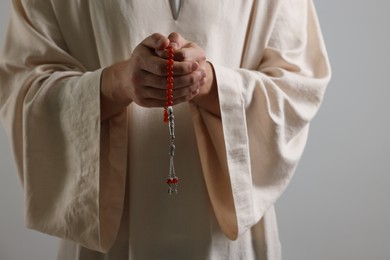 Photo of Muslim man with misbaha praying on light grey background, closeup