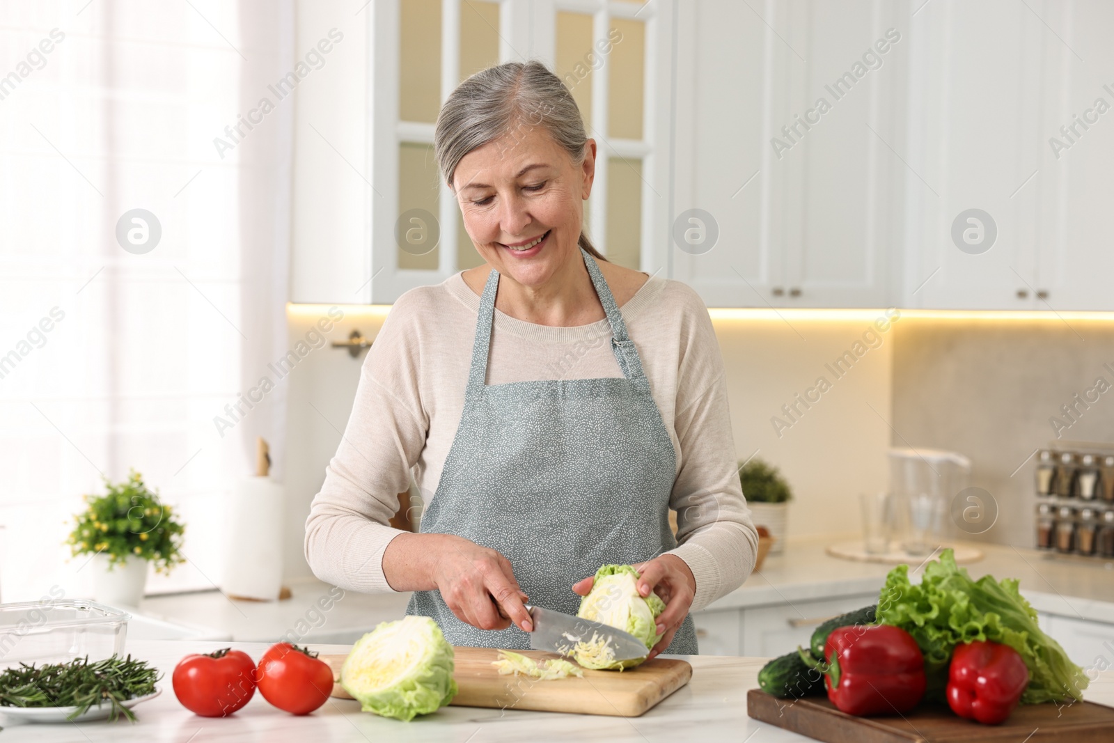 Photo of Happy housewife cutting cabbage at table in kitchen